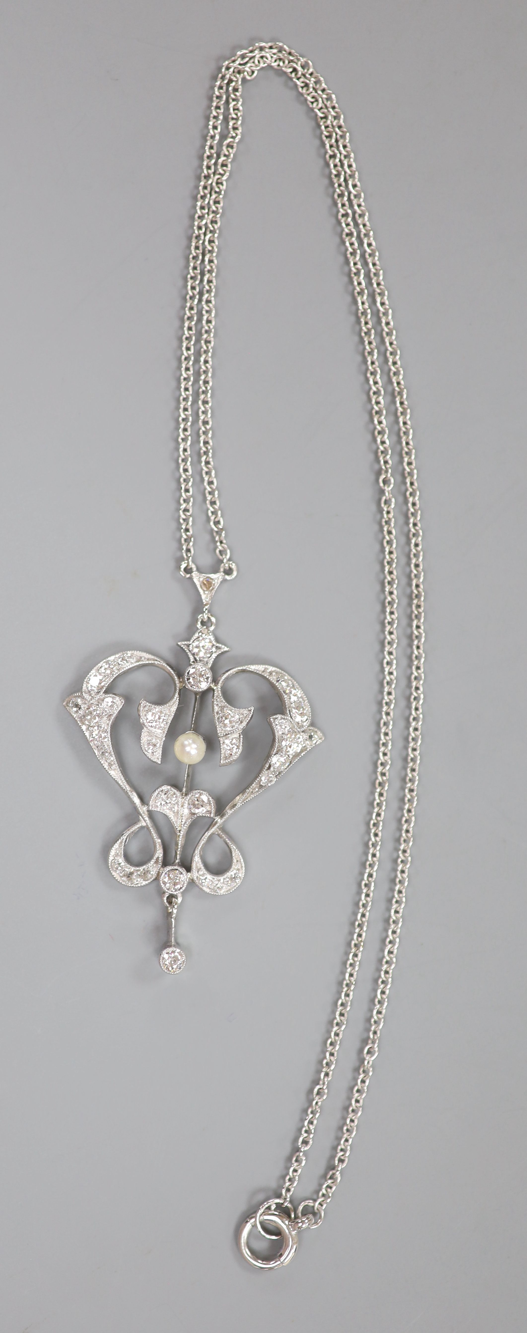 An Art Nouveau style white metal seed pearl and diamond set openwork scroll drop pendant necklace, pendant 4cm, chain 40cm,